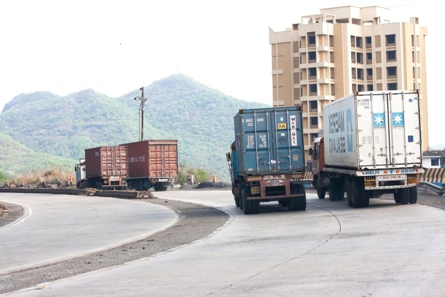 Container trucks on a curving highway with hills behind, similar to the long carrier route from Gurgaon to Pune